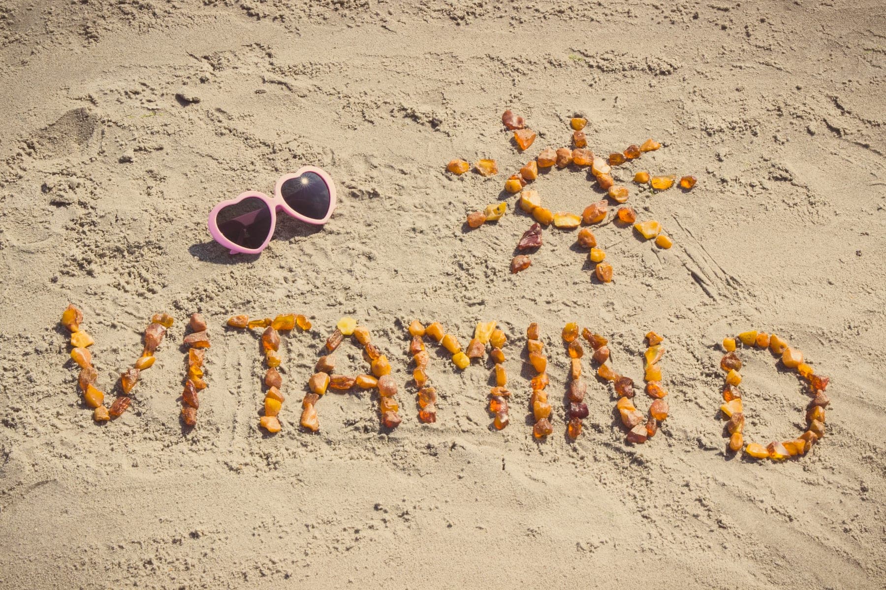 Schriftzug „Vitamin D" aus Steinen im Sand – Ratgeber vom Members Club, Sonnenstudio & Solarium in Hamburg